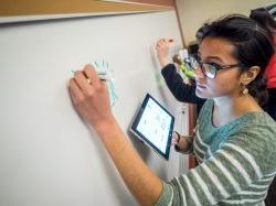 Photo of student writing Chinese characters from her tablet onto whiteboard.