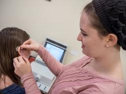 Photo of an audiology student fitting a hearing aid